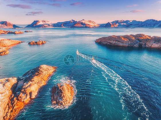 鸟瞰渔船,蓝色海洋中的岩石,雪山五颜六色的紫色天空,冬季的黄昏,挪威洛弗滕岛,两艘船的景观的风景旅行空中俯图片