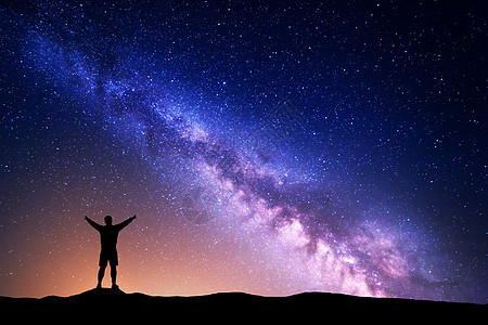 紫色的银河,个站着的人的轮廓,举手臂山上美丽的星系的夜景宇宙夜空中银河黄光图片