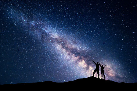 银河系夜空中星星轮廓,站山上的快乐的男人女人举手臂蓝色的银河山上的人宇宙的背景夜风景图片
