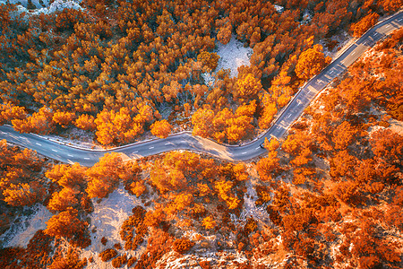 空中观看山曲线道路与汽车,橙色森林日落欧洲秋季景观与沥青道路,树木岩石上穿过公园的高速公路飞行无人机的顶部视图图片