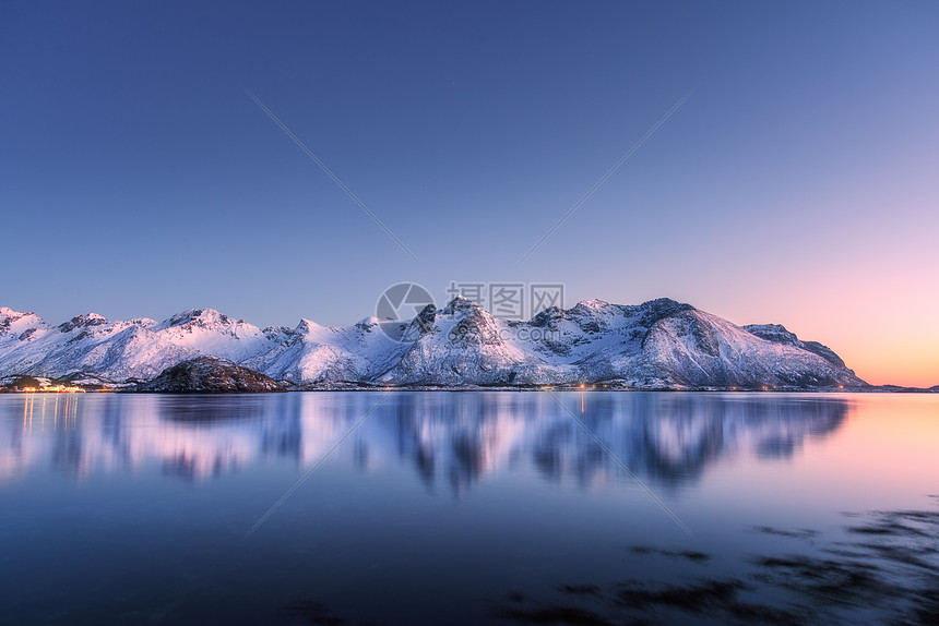 美丽的雪覆盖着群山,五彩缤纷的天空夜晚反射水中冬季景观海洋,雪岩,蓝天,倒影,日落时的阳光黄昏时分,挪威的洛芬岛图片