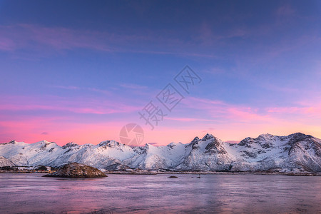 美丽的雪覆盖着群山,五彩缤纷的天空夜晚反射水中冬季景观海洋,雪岩,天空,粉红色的云,日落时的倒影黄昏时分,挪威的洛图片