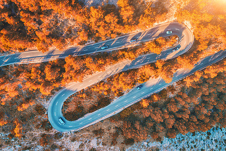 空中观看山曲线道路与汽车,橙色森林日落欧洲秋季景观与沥青道路,树木岩石上穿过公园的高速公路飞行无人机的顶部视图图片