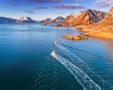 鸟瞰渔船,蓝色海洋中的岩石,雪山五颜六色的天空,冬季的洛福滕岛,挪威,景观与两艘船日落的风景旅行海景图片