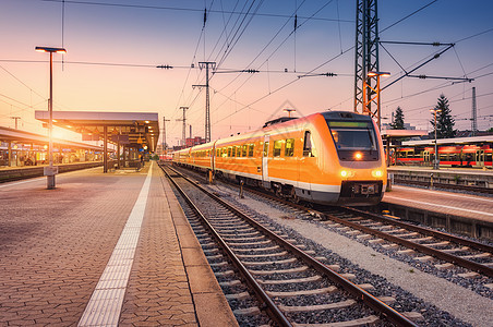 日落时火车站上的橙色高速列车城市景观与现代通勤列车铁路站台上,黄昏的五彩缤纷的天空欧洲铁路上的客运车辆图片
