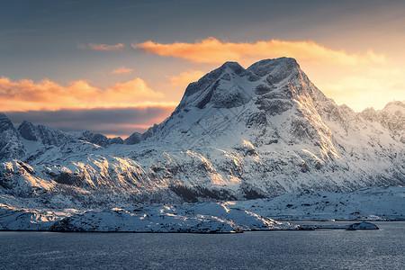 雄伟的景象,美丽的高雪覆盖了冬天日落时的山脉挪威洛福腾群岛风景与雪岩,海洋,橙色的天空与云阳光晚上旅行图片