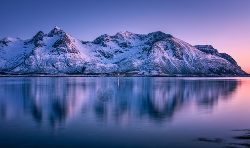 美丽的雪覆盖着群山,五彩缤纷的天空黄昏时反射水中冬季景观与海洋,雪岩,紫色的天空,倒影,日落洛芬岛,挪威黄昏自背景图片