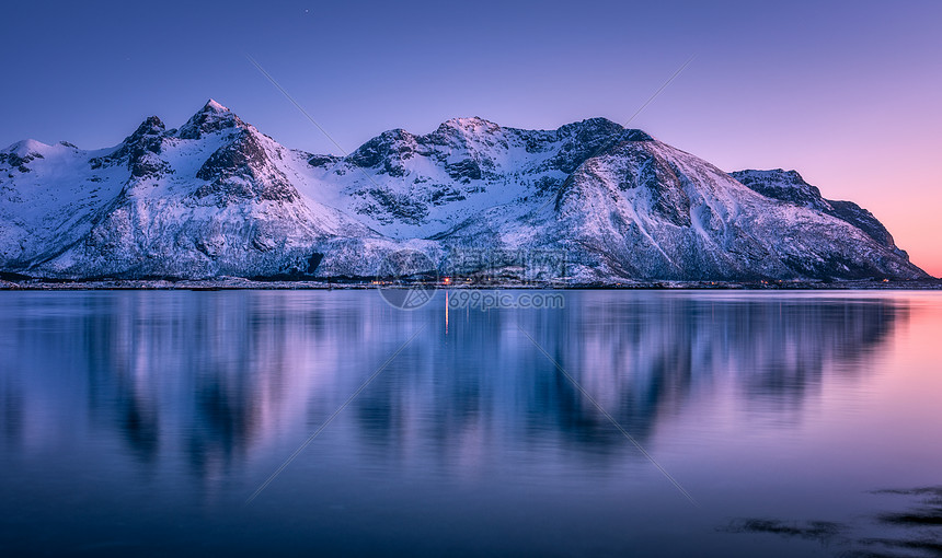 美丽的雪覆盖着群山,五彩缤纷的天空黄昏时反射水中冬季景观与海洋,雪岩,紫色的天空,倒影,日落洛芬岛,挪威黄昏自图片