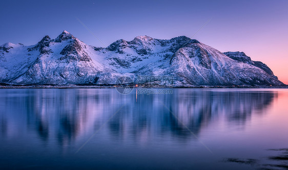 美丽的雪覆盖着群山,五彩缤纷的天空黄昏时反射水中冬季景观与海洋,雪岩,紫色的天空,倒影,日落洛芬岛,挪威黄昏自图片