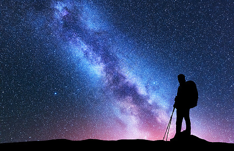 夜晚,带着背包徒步旅行杆的男人令人惊叹的紫色银河上的剪影风景与人,明亮的银河,天空与星星美丽的星系旅行图片
