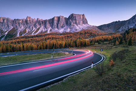 模糊的汽车前灯蜿蜒的沥青道路上,秋天的日落壮观的景观,灯光小径,森林,岩石紫色的天空秋天的夜晚汽车路上行驶图片