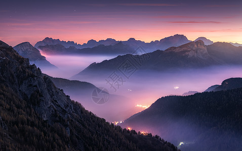 美丽的夜晚雾中的山脉秋天的白云石,意大利景观与高山山谷,低云,森林,紫色的天空与星星,城市照明日落空中飞行帕索图片