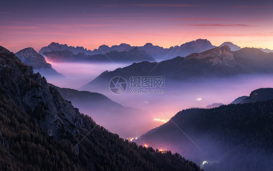 美丽的夜晚雾中的山脉秋天的白云石,意大利景观与高山山谷,低云,森林,紫色的天空与星星,城市照明日落空中飞行帕索图片