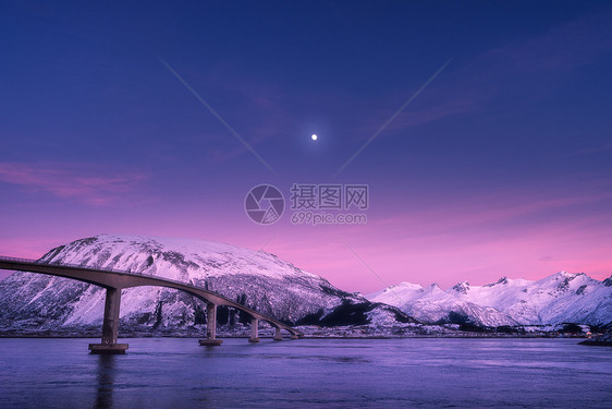 美丽的桥抵雪山,紫色的天空,粉红色的云彩月亮夜间洛福滕岛,挪威冬天的风景道路,蓝色的大海,雪覆盖的岩石黄昏欧洲图片