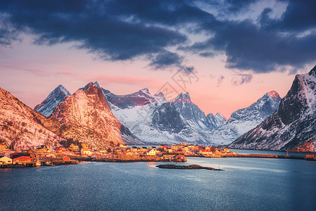 冬天美丽的日出时,雷恩村雪覆盖着群山挪威洛福腾群岛景观蓝色的海洋,雪岩,房屋传统的罗布斯,五颜六色的天空与云图片