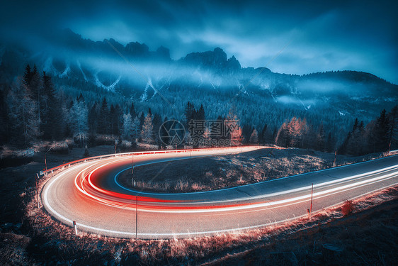 模糊的汽车前灯蜿蜒的道路上,秋天的夜晚,云层很低昏暗的景观与沥青路,轻小径,雾林,岩石蓝天黄昏意大利的巷道图片