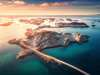 挪威洛福滕岛海上山脉上的桥梁的鸟瞰图亨宁斯娃冬天的日落景观与蔚蓝的水,天空与金色的阳光,岩石,建筑物,道路的图片