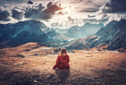 轻的女人坐田野上,意大利白云石的秋天日落时,着雄伟的山脉风景与女孩,多云的天空,橙色的草,高岩石与森林秋天意大图片