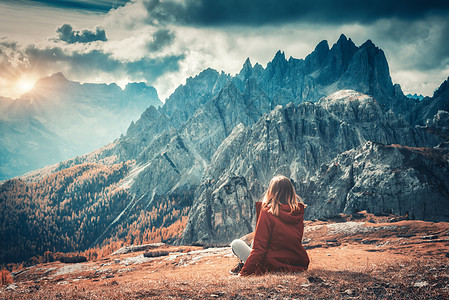轻的女人正坐山上,秋天的白云石,意大利的壮丽的山风景与女孩,多云的天空,橙色的草,高岩石与森林秋天意大利阿尔卑斯图片