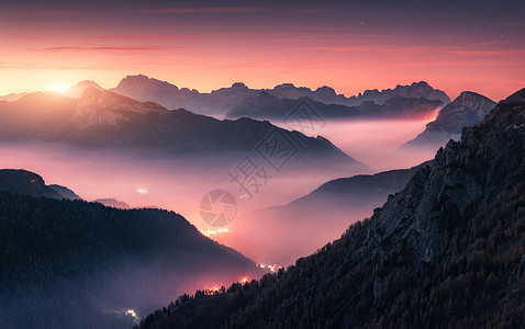 意大利白云石秋天美丽的日落时,雾中的山脉景观与高山山谷,低云,森林,紫色天空城市照明黄昏空中视野帕索贾乌图片