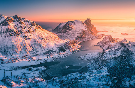 挪威洛福滕群岛日落时美丽峡湾的鸟瞰图冬天的风景雪山,蔚蓝的大海金色的阳光雪中岩石的顶部景观,村庄北部海岸线图片