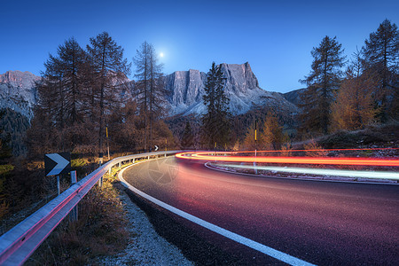 秋天的夜晚,蜿蜒的道路上模糊的汽车前灯风景与沥青道路,轻小径,山脉,树木,蓝天与月亮黄昏意大利的巷道看公路岩石图片