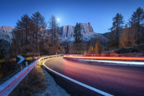 秋天的夜晚,蜿蜒的道路上模糊的汽车前灯风景与沥青道路,轻小径,山脉,树木,蓝天与月亮黄昏意大利的巷道看公路岩石图片