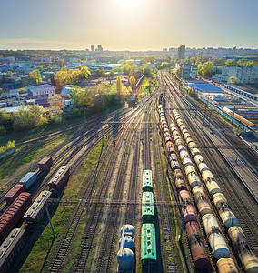 日落时火车站彩色货运列车的鸟瞰图铁路上货物的货车重工业货运列车城市建筑蓝天的工业场景无人机的顶部视图图片