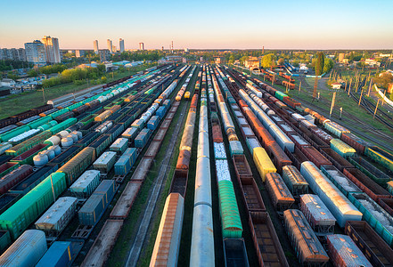 日落时火车站彩色货运列车的鸟瞰图铁路上货物的货车重工业货运列车城市建筑蓝天的工业场景无人机的顶部视图图片
