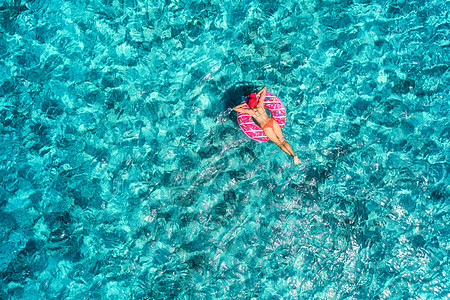 阳光明媚的日子里,苗条的轻女子透明的蓝色海洋中的粉红色甜甜圈游泳圈上游泳热带航空景观与女孩,蔚蓝的水的风景图片