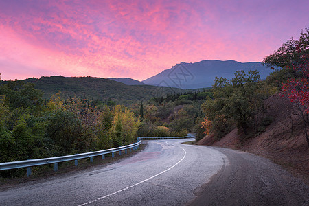 蜿蜒的山路穿过森林,夏天的日落时,天空红云充满了戏剧的色彩图片