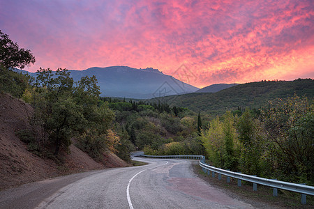 蜿蜒的山路穿过森林,夏天的日落时,天空红云充满了戏剧的色彩图片