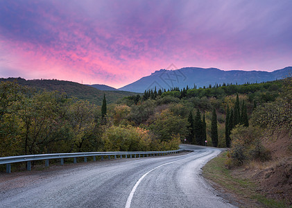 山蜿蜒的道路穿过森林,五颜六色的天空粉红色的云夏天的日落图片