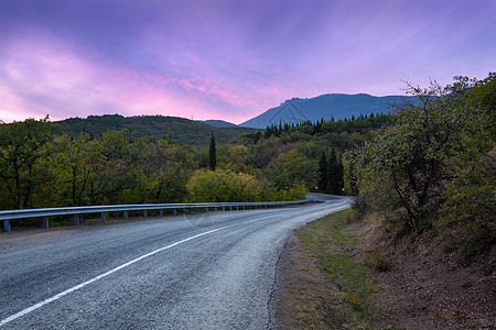 山蜿蜒的道路穿过森林,夏天的日落时,天空五彩缤纷图片