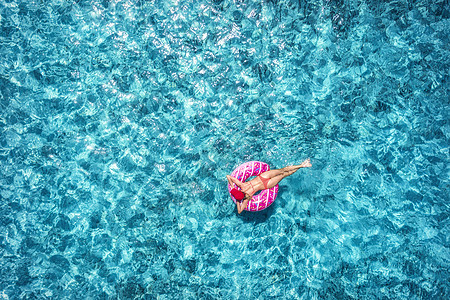 鸟瞰苗条的轻女子游泳粉红色甜甜圈游泳环清澈的蓝色海洋阳光明媚的夏天热带航空景观与女孩,蔚蓝的水无人机的顶部视图图片
