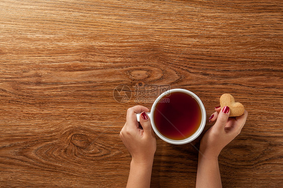 女人着杯热茶,木桌上放着饼干图片