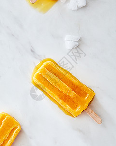 橙色水果冰淇淋棍子上,灰色大理石背景上冰片,文字夏季甜点的平躺橙色融化的冰淇淋与冰片灰色大理石桌子图片