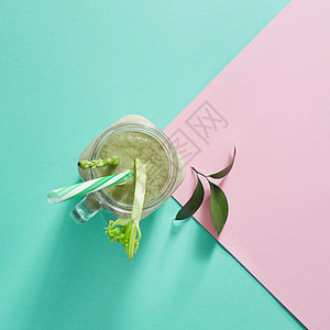 素食健康冰沙绿色蔬菜与绿叶塑料吸管个璃碗上的双调粉红色绿纸背景俯视图绿色机蔬菜与芦笋芹菜个璃碗上的双图片
