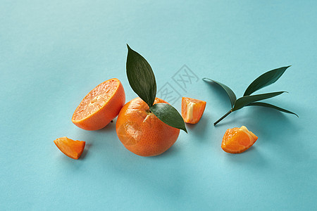 热带异国情调的柑橘类水果曼达林整体切片与绿叶蓝色的纸张背景异国情调的柑橘类水果,绿叶蓝色的纸上图片