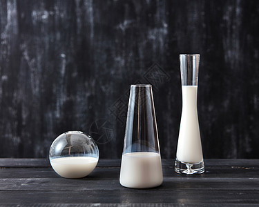 璃花瓶里的白色牛奶放个黑色的木制桌子上,背节省牛奶的乳制品同形状的璃容器中,黑色背景上牛奶图片