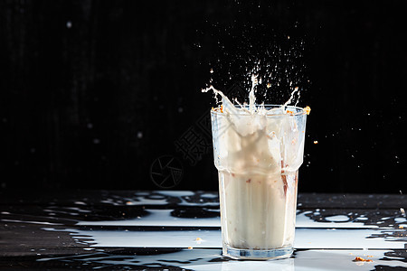 用燕麦米斯利璃上溅牛奶,把牛奶洒张黑色的木桌上,文字的位置牛奶白色液体飞溅燕麦片,黑色背景上的璃中溅出图片