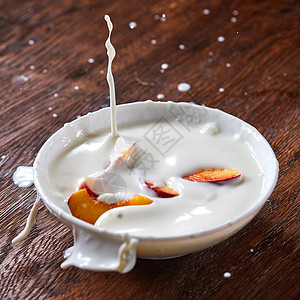 牛奶酸奶溅同的方向,成熟的桃子水果掉进陶瓷碗里准备顿美味健康的早餐片成熟的新鲜桃子落陶瓷碗里,张木桌上放了图片