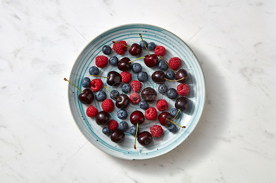 夏天美味的水果浆果蓝色盘子上的灰色混凝土背景清洁机饮食的平躺美味的甜樱桃,蓝莓,覆盆子蓝色盘子上的灰色大理石图片