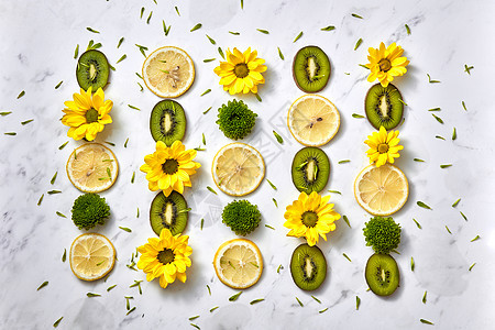 种均匀排列的图案,由黄色绿色的花水果猕猴桃柠檬片绿色花瓣成花卉构图,花卉背景的风景花卉背景花型图片
