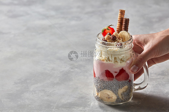 杯女士手中手柄的璃杯,配上健康的酸奶早餐草莓加香蕉的奇亚布丁装饰饼干奶油的灰色混凝土背景璃与分图片