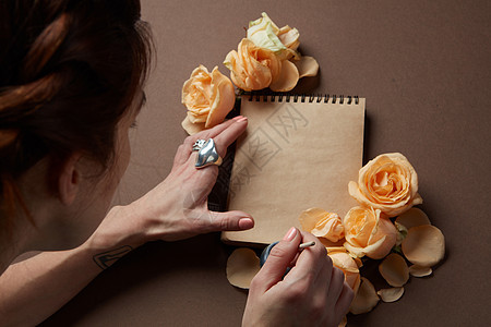 女人用橙色玫瑰记事本上写着爱的标志用画笔写情书图片