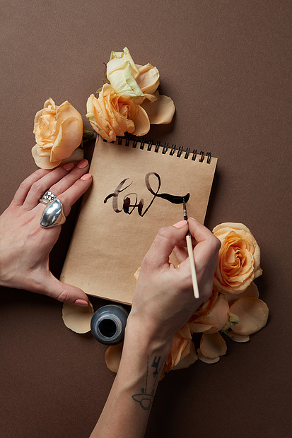 女人白纸上写着爱词,棕色的背景上写着花顶部视图用钢笔写字图片