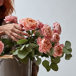 个穿着棕色围裙的女人着个花瓶粉红色的媒体玫瑰的特写母亲节花店与着花瓶玫瑰的女孩图片