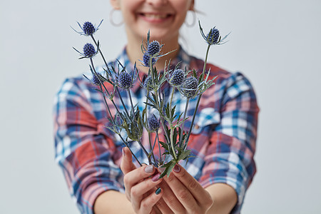 带着蓝色花朵的轻微笑的女孩女人手握灰色背景,母亲节轻的女孩着朵蓝色的花图片