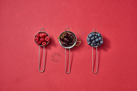 红色成熟多汁浆果樱桃,覆盆子,蓝莓红纸背景与健康的机五颜六色的食物图案与三个颜色与红色多汁成熟樱桃,图片